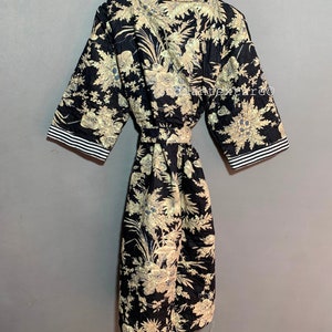 May include: A black quilted robe with a floral pattern in beige and blue. The robe has short sleeves with white and black striped trim, a matching belt, and is hanging on a wooden hanger.