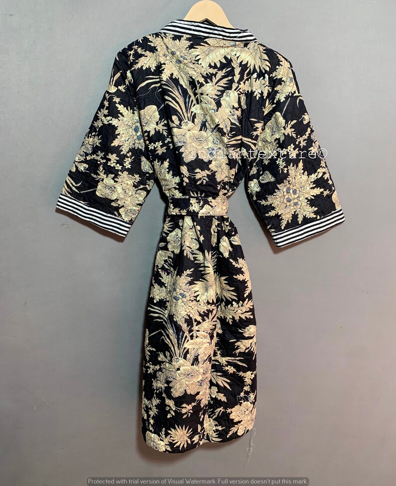May include: A black quilted robe with a floral pattern in beige and blue. The robe has short sleeves with white and black striped trim, a matching belt, and is hanging on a wooden hanger.
