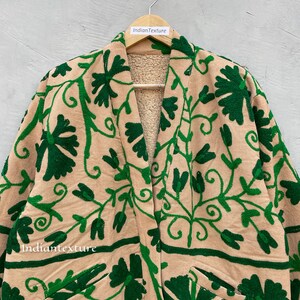 Op de afbeelding: Een beige geborduurde jas met groene bloemenborduursel. De jas heeft een shawlkraag en twee zakken. De tekst "Indiantexture" is zichtbaar op de jas.