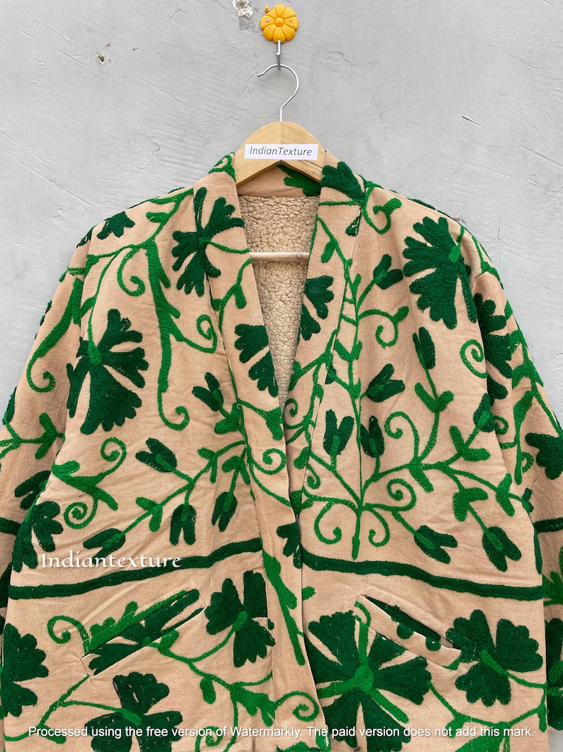 Op de afbeelding: Een beige geborduurde jas met groene bloemenborduursel. De jas heeft een shawlkraag en twee zakken. De tekst "Indiantexture" is zichtbaar op de jas.