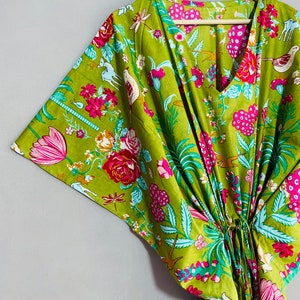Peut inclure: Un kaftan en coton vert &agrave; imprim&eacute; floral avec des fleurs roses, blanches et bleues, des oiseaux et d'autres motifs. Le kaftan a un col en V et une ceinture &agrave; la taille. Le texte "INDIAN TEXTURE" est imprim&eacute; sur un cintre en bois.