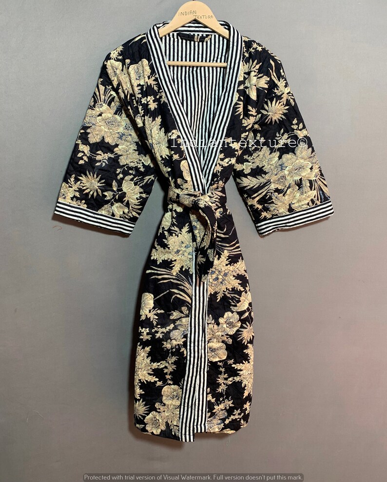 May include: A black floral print robe with a striped interior and trim. The robe features a tie closure and is displayed on a wooden hanger. The floral pattern includes beige and light blue accents.