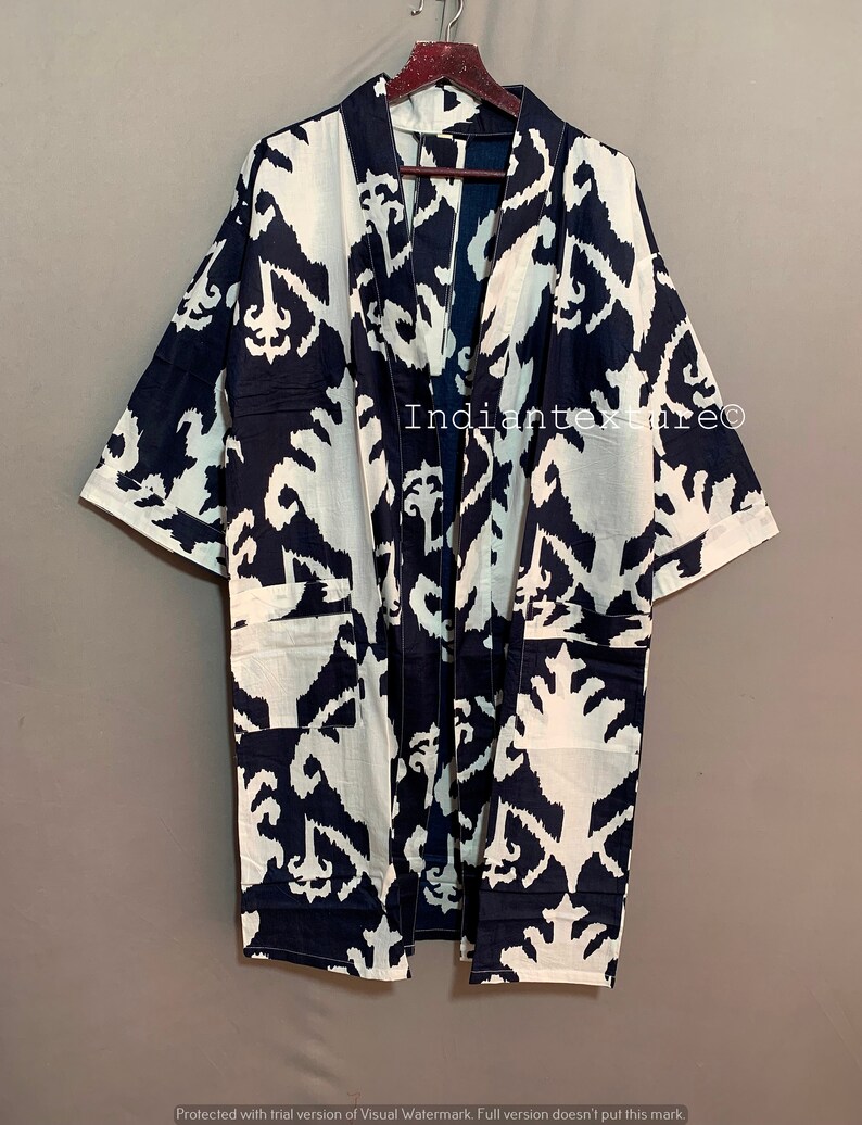 May include: A long, black and white kimono with an ikat pattern. The kimono has a wide collar and long sleeves. The fabric is soft and flowing.