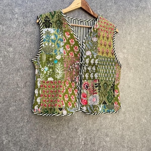 May include: A green quilted vest with a floral print and a tie closure. The vest is made of cotton and has a patchwork design.