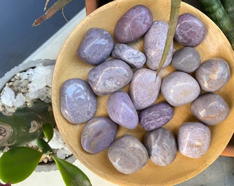 May include: A collection of smooth, polished purple and white stones in a wooden bowl. The stones have a natural, organic look and feel.