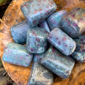 Peut inclure: Une collection de pierres de zoïsite rubis roulées. Les pierres sont un mélange de couleurs bleues, vertes et rouges. Elles sont lisses et polies.