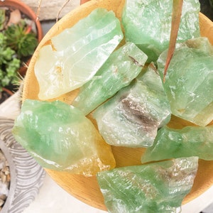 May include: A collection of green and yellow crystal chunks on a wooden surface. The crystals are rough and have a natural, unpolished look.