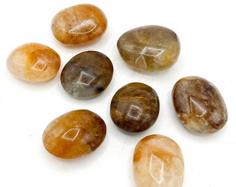 Puede incluir: Ocho piedras lisas de forma ovalada en tonos naranja, marrón y blanco. Las piedras están pulidas y tienen un aspecto natural y terroso.