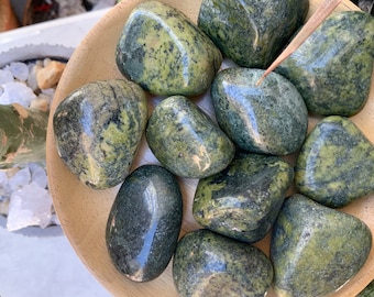 May include: A collection of eight green and black serpentine tumbled stones in a wooden bowl. The stones are smooth and polished, with a variety of patterns and swirls.