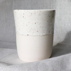 May include: A white ceramic mug with a black handle and the text "But First, Coffee" in a bold, black font. The mug is set against a blurred background, highlighting its clean design.