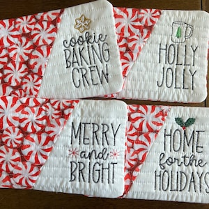May include: Four white quilted pot holders with red and white peppermint candy designs. The pot holders have different embroidered sayings: "Cookie Baking Crew", "Holly Jolly", "Merry and Bright", and "Home for the Holidays".