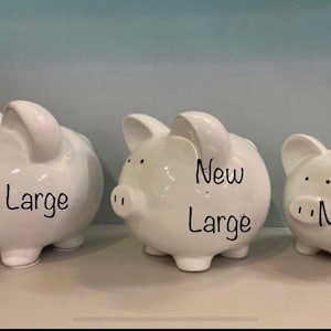 May include: Three white ceramic piggy banks of different sizes. The largest piggy bank says "Large" on it. The middle piggy bank says "New Large" on it. The smallest piggy bank says "Medium" on it.
