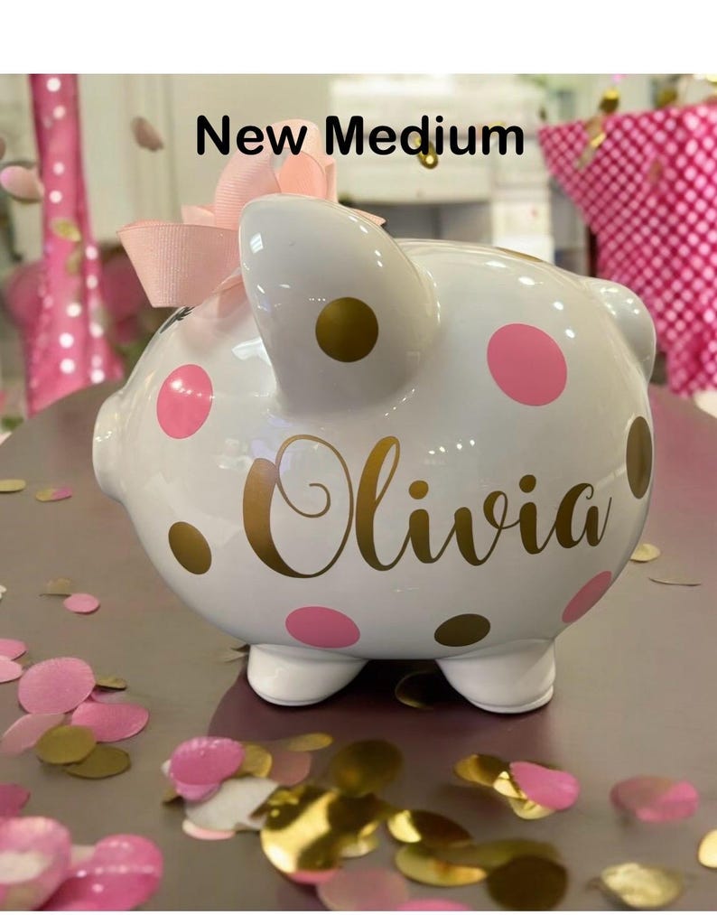 May include: White ceramic piggy bank with pink and gold polka dots. The piggy bank has the name "Olivia" written in gold lettering.