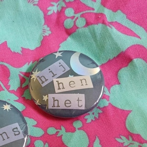 Peut inclure: Un bouton bleu foncé avec un croissant de lune et des étoiles. Les mots "hij", "hen" et "het" sont imprimés sur le bouton.