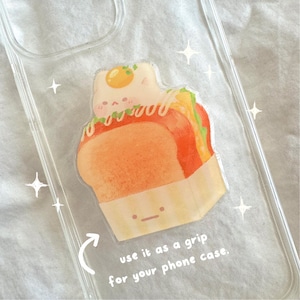 May include: A clear phone case with a cartoon illustration of a sandwich with a cute face. The text "use it as a grip for your phone case." is printed on the case.