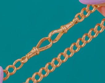 Könnte beinhalten: Nahaufnahme einer goldfarbenen Kette mit Verschluss. Die Kettenglieder sind im abgerundeten Curb-Stil gehalten. Der Verschluss ist ein dekoratives Element mit Haken und Stange. Der Hintergrund ist einfarbig türkis.