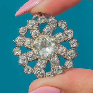 May include: A silver pendant with a large, clear, faceted gemstone surrounded by smaller, clear, faceted gemstones. The pendant is in the shape of a flower with eight petals.