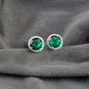 Può includere: Un paio di orecchini d'argento con pietre ovali di colore verde smeraldo circondate da un alone di piccole pietre trasparenti.