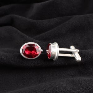 May include: A pair of silver cufflinks with red oval-shaped gemstones.