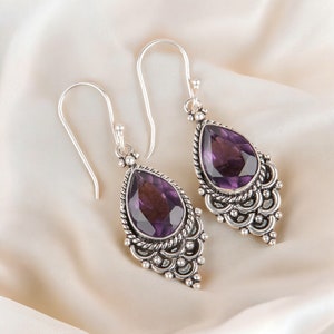 May include: A pair of silver dangle earrings with intricate detailing and a pear-shaped amethyst gemstone in each earring.