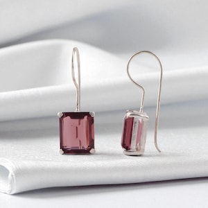 May include: Silver drop earrings with rectangular, pink gemstones. The earrings have a hook closure. The gemstones are set in a silver bezel setting. The earrings are a classic design, suitable for everyday wear or special occasions.