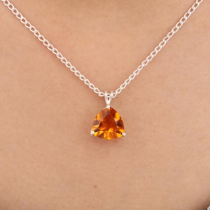 Può includere: Una collana con catena d'argento con un pendente triangolare di pietra preziosa arancione. Il pendente è di un colore arancione caldo e vibrante ed è incastonato in una lunetta d'argento. La catena è a maglie delicate.