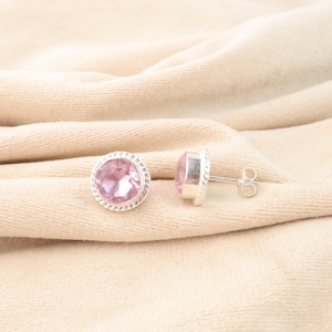Peut inclure: Une paire de boucles d'oreilles en argent avec des accents de pierres précieuses roses. Les boucles d'oreilles sont rondes et ont une bordure délicate en forme de corde.