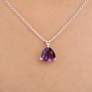 Op de afbeelding: Een zilveren ketting met een driehoekige, dieppaarse edelsteen hanger. De hanger is gezet in een zilveren bezel en de ketting heeft een delicate schakelstijl. De edelsteen heeft een facetgeslepen slijpvorm.