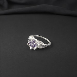 May include: A silver ring with a purple gemstone set in a flower design.
