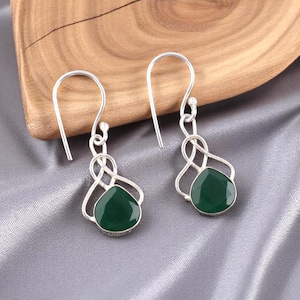 Op de afbeelding: Zilveren oorhangers met donkergroene, druppelvormige edelstenen. De oorbellen hebben een decoratief zilveren filigraanontwerp rond de groene stenen en een eenvoudige haaksluiting. De oorbellen worden op een grijze ondergrond getoond.