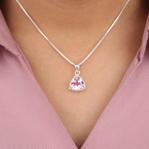 Puede incluir: Un collar de cadena de plata con un colgante triangular con una piedra preciosa rosa.