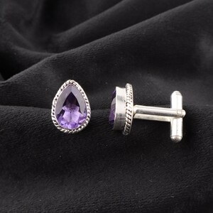 May include: A pair of silver cufflinks with purple amethyst stones. The stones are set in a pear shape and have a silver border.