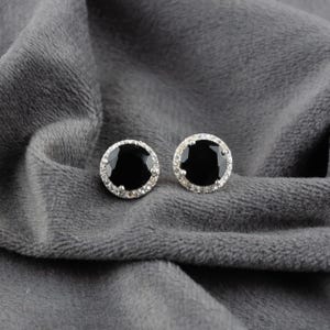 May include: A pair of silver earrings featuring black oval-shaped gemstones with a halo of smaller clear gemstones.