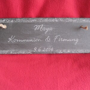 Könnte beinhalten: Eine schwarze Schiefertafel mit einer weißen Inschrift, die "Maya Kommunion & Firmung 9.6.2014" lautet. Die Tafel hat einen dekorativen Rand und ist mit einer Schnur gebunden.
