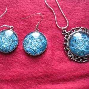 May include: A set of silver tone jewelry with blue and white paisley patterned glass cabochons. The set includes a necklace and a pair of earrings.
