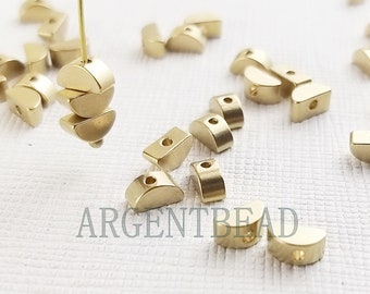 May include: A collection of gold-toned metal half-circle beads with a hole in the center. The beads are scattered on a white surface.