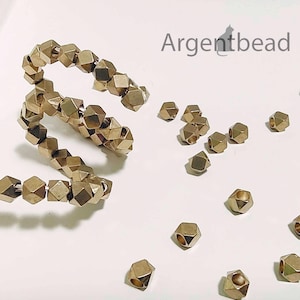 May include: A close-up of gold-toned metal beads with a faceted, geometric design. The beads are arranged in a spiral pattern and scattered on a white surface. The text "Argentbead" is visible in the top right corner of the image.