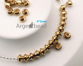 Pode incluir: Um close-up de contas de metal douradas, algumas enfiadas em um fio de prata. As contas têm 4 mm de diâmetro e um design facetado. O texto "4*2mm Argentbead" é visível na imagem.