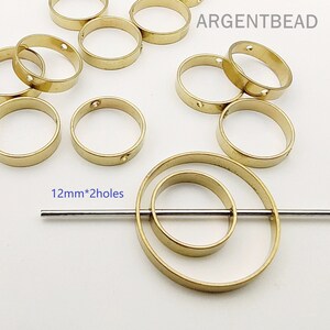 May include: A selection of gold-coloured metal rings, some with small holes, are arranged on a white surface. The rings are approximately 1.2cm in diameter. The text "ARGENTBEAD" is visible in the upper right corner.