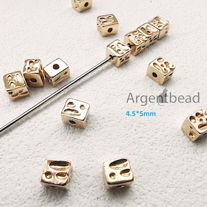 Może przedstawiać: Złote metalowe koraliki w kształcie sześcianu z fakturowaną powierzchnią i otworem w środku. Koraliki mają rozmiar 4,5 x 5 mm. Argentbead.