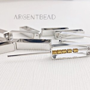 May include: Silver metal bead spacers with a row of gold beads in the center. The spacers are rectangular and have a slightly rounded edge. The gold beads are small and round.