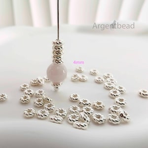 May include: A selection of silver-coloured jewellery-making beads. The image shows a strand of beads with a pink gemstone and several small, round, textured beads. The text "4mm" is visible, indicating the size of the beads. The brand name "Argentbead" is also visible.