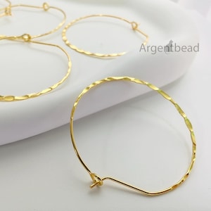 May include: Close-up of several gold-colored hoop earrings. The earrings have a hammered texture and a simple hook closure. The brand name "Argentbead" is visible in the background. These earrings are a classic jewelry accessory.