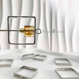 May include: A square metal bead frame holds a faceted, amber-coloured gemstone. Several other square metal frames are scattered on a white surface. The Argentbead logo is visible in the background.