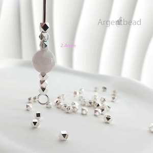 May include: A vertical strand of jewelry components featuring a large, smooth, pale pink spherical bead flanked by small, faceted, metallic silver-colored beads. The text 2.4mm is visible, indicating the size of the faceted beads. Argentbead is printed.