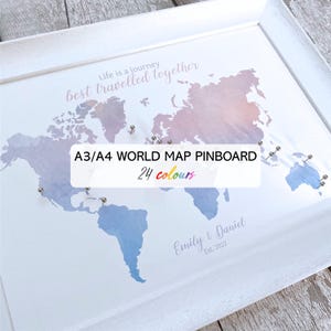 May include: A framed world map pinboard with a white frame. The map features blue and pink hues, with pins indicating locations. The text "Life is a journey best travelled together" is displayed. The text "A3/A4 WORLD MAP PINBOARD 24 colours" is also visible.