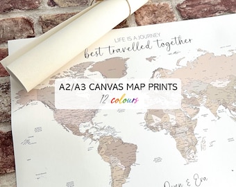 May include: A world map canvas print with the text "Life is a journey, best travelled together." The map is in neutral tones, with the text "A2/A3 CANVAS MAP PRINTS, 12 colours." A rolled canvas is tied with twine. The names "Owen & Eva" and the year "Est. 2021" are also visible.