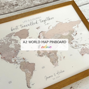 May include: A framed A2 world map pinboard with a light brown frame. The map features a neutral color palette with pins marking locations. Text on the map includes "LIFE IS A JOURNEY best travelled together", "A2 WORLD MAP PINBOARD 8 colours", and a personalized inscription.
