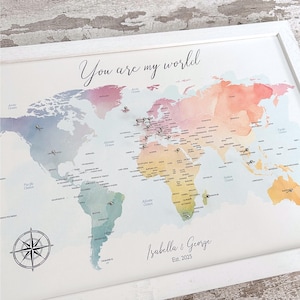 May include: A framed world map with a watercolour design in pastel shades of pink, blue, yellow, and green. The text "You are my world" is at the top. The names "Isabella & George" and the year "Est. 2025" are at the bottom.