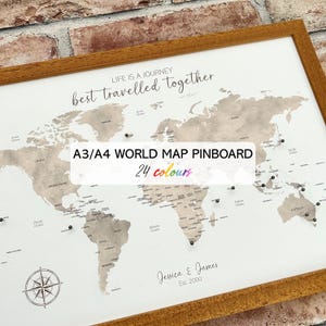 May include: A framed world map pinboard with a light brown wooden frame. The map is in neutral tones with pins marking locations. Text on the map reads "Life is a journey, best travelled together." The text "A3/A4 WORLD MAP PINBOARD 24 colours" is also visible.